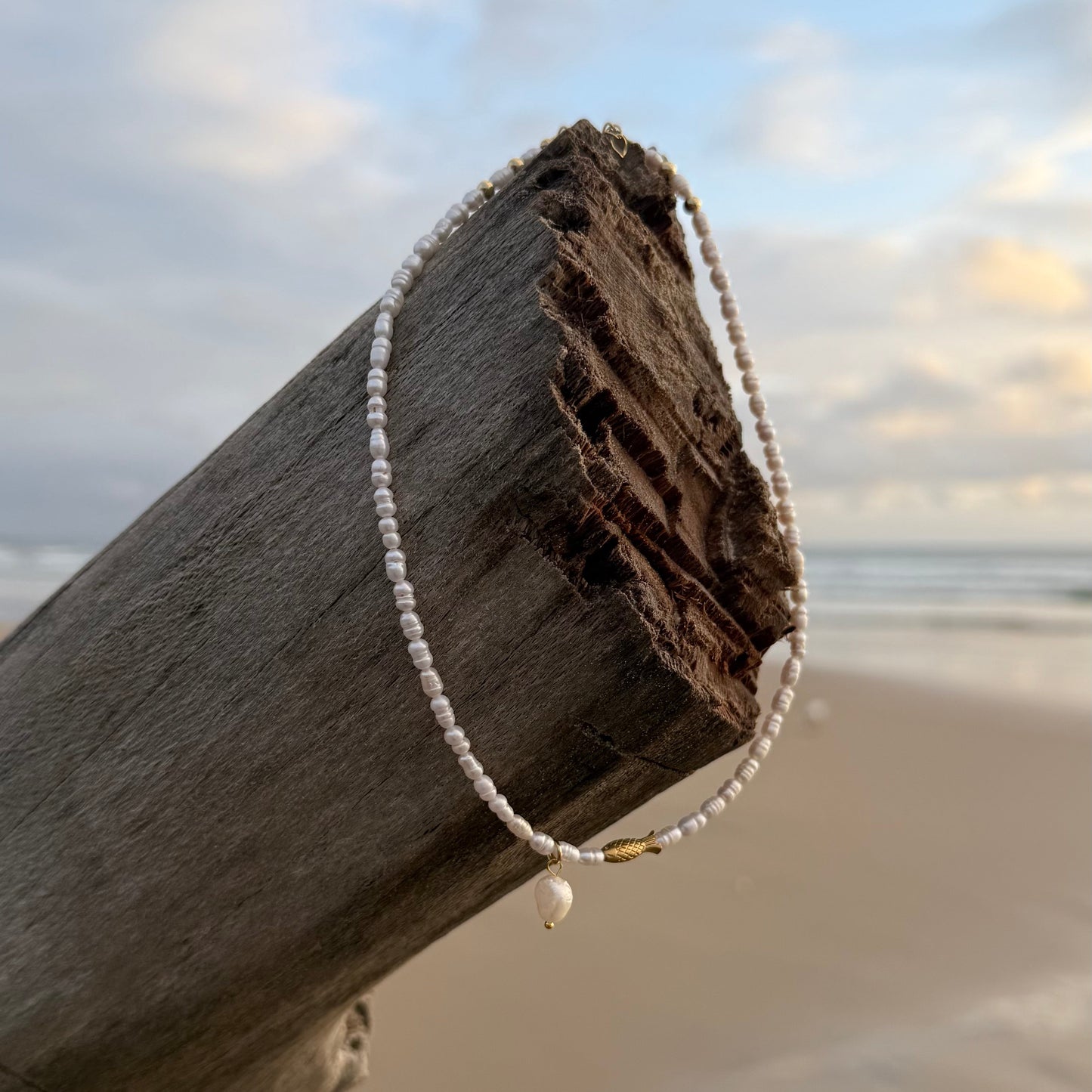 Pearl bracelet draped over a wooden post on a beach with ocean and sky in the background