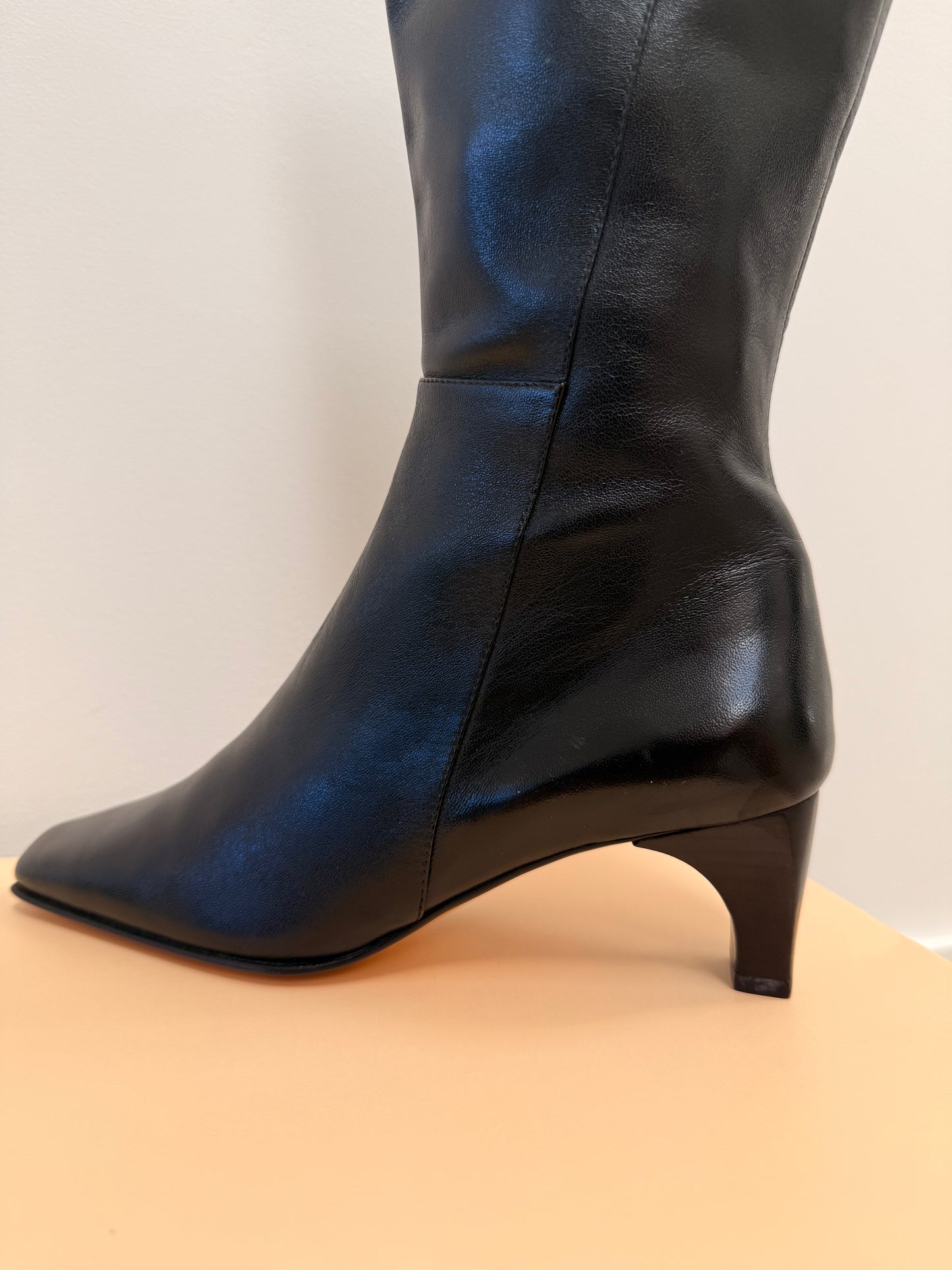 Black knee-high boots on a beige platform with a neutral background